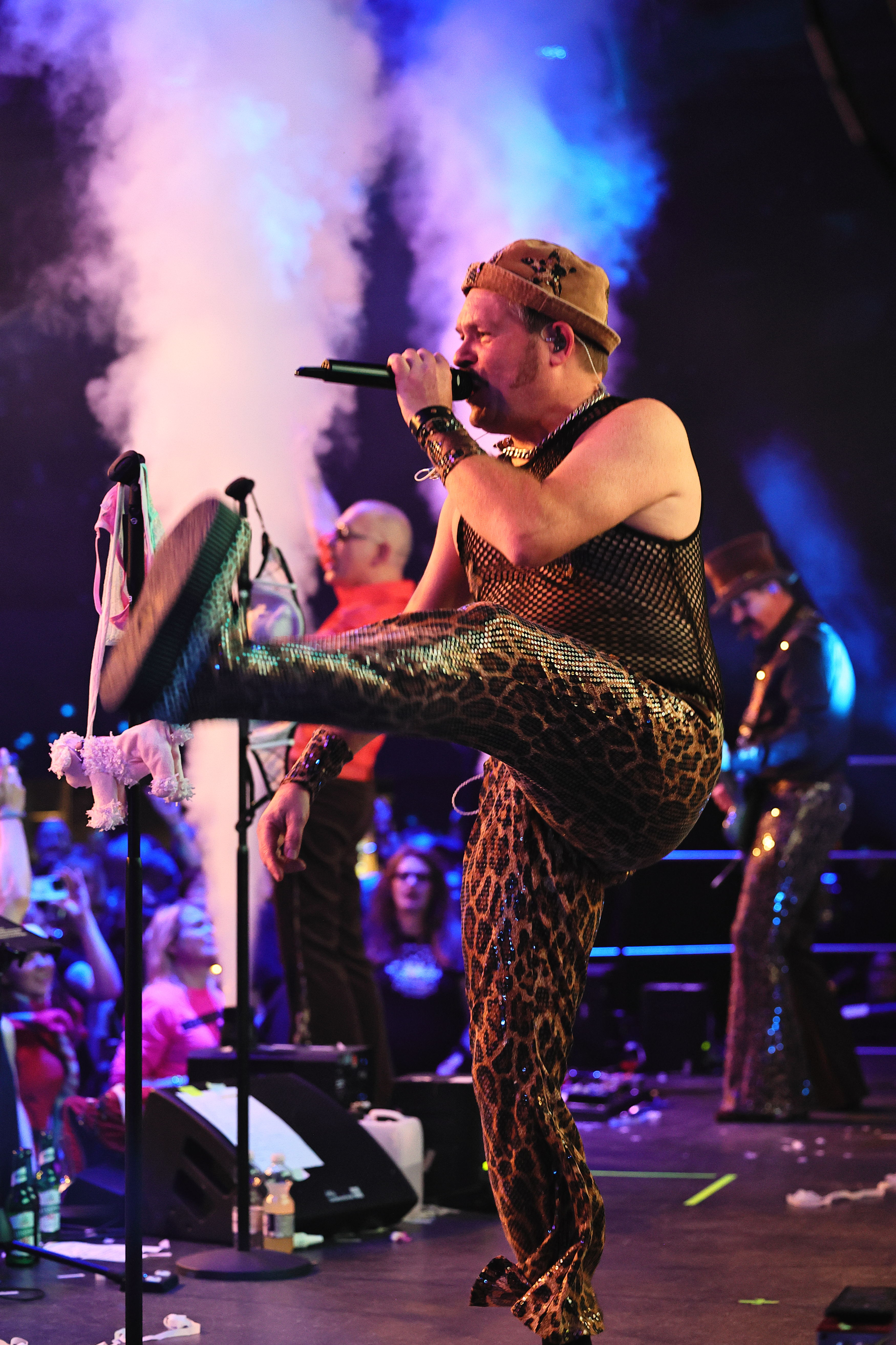 Sänger ruft ins Mikrofon, Nebeleffekt steigt neben ihm auf.