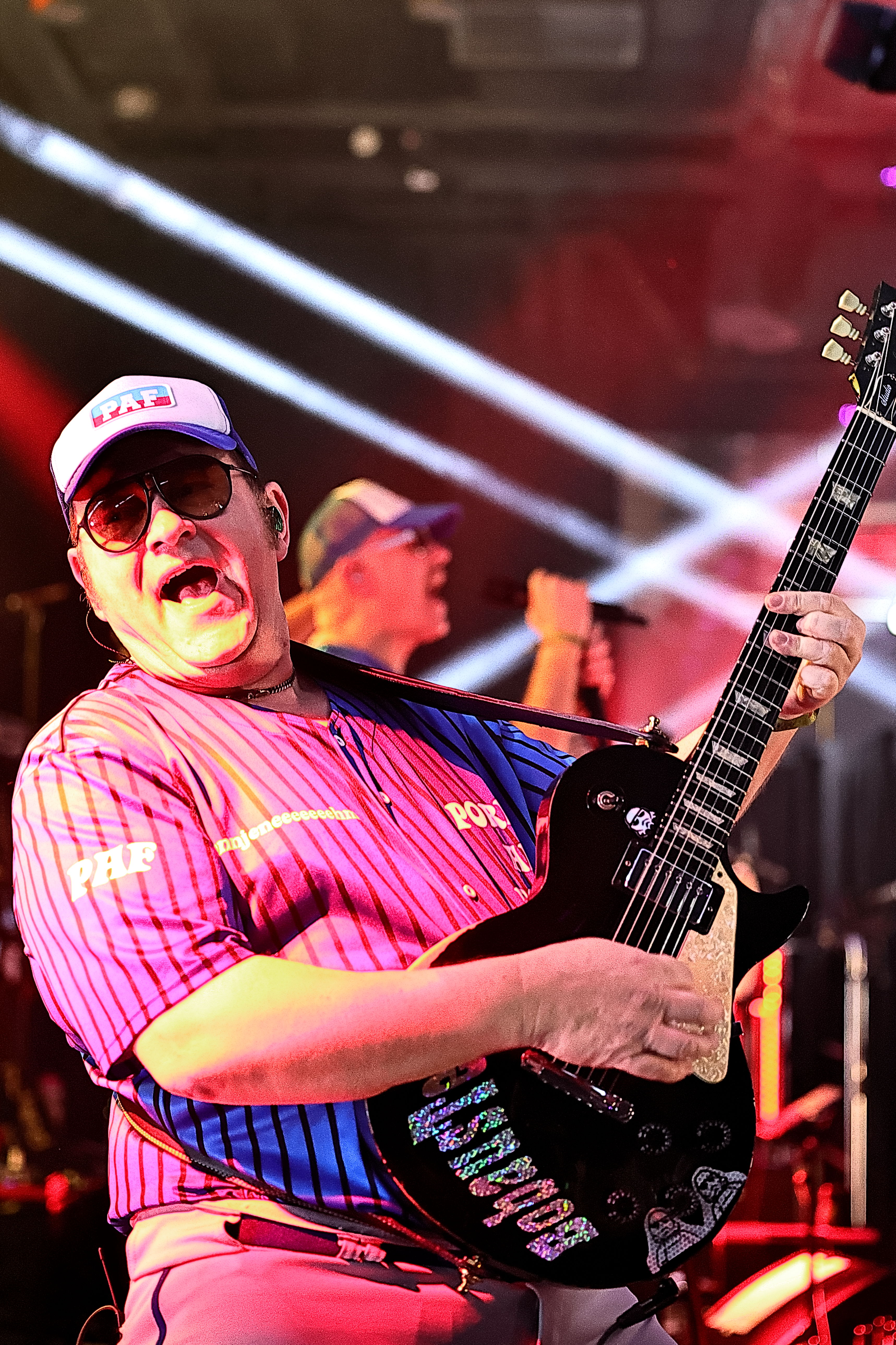 Gitarrist im pinken Outfit spielt, Bühne in rotem Licht.