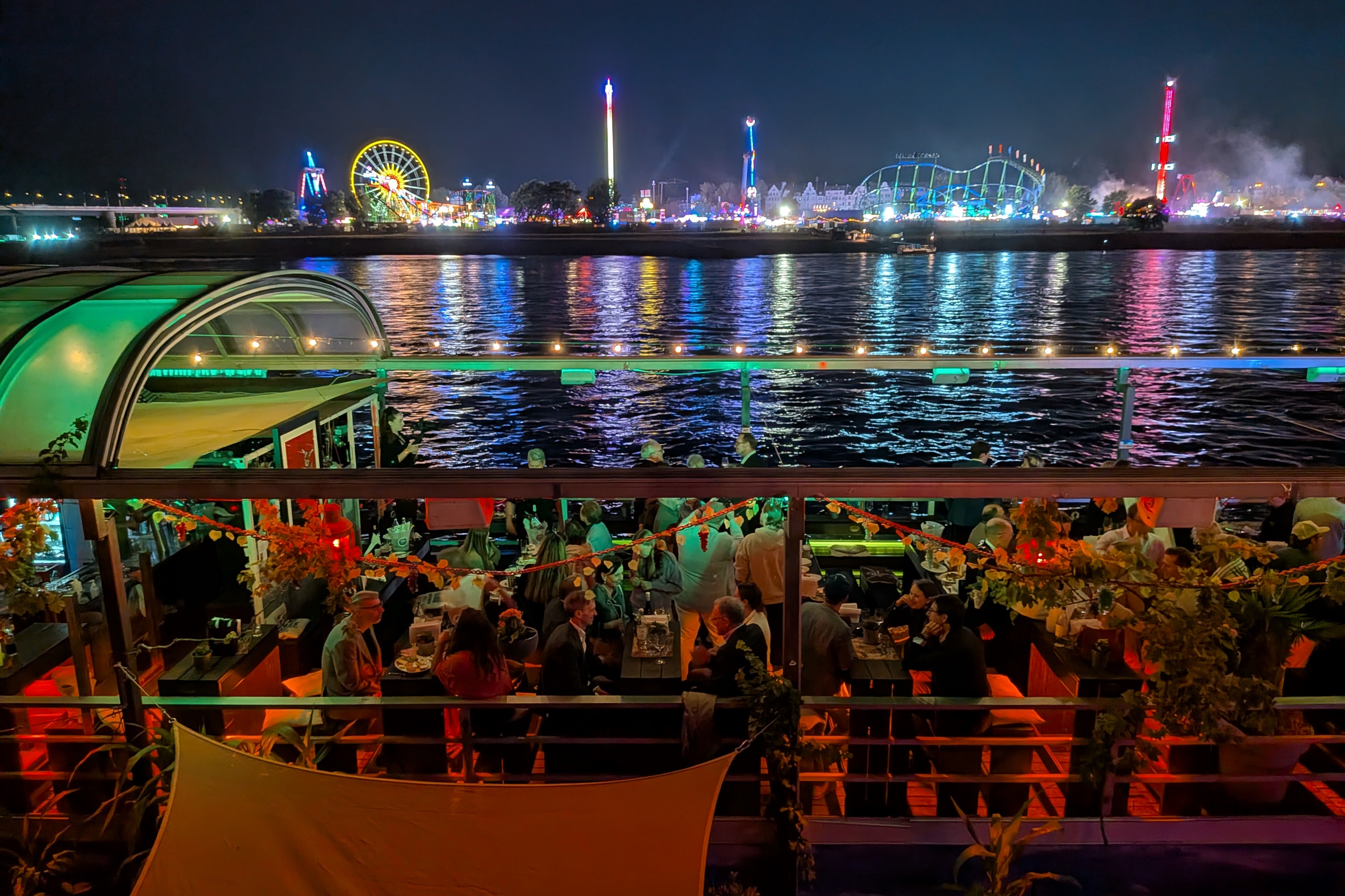 Blick vom gut besuchten Deck der MS Allegra über den Rhein auf die beleuchtete Rheinkirmes in Düsseldorf