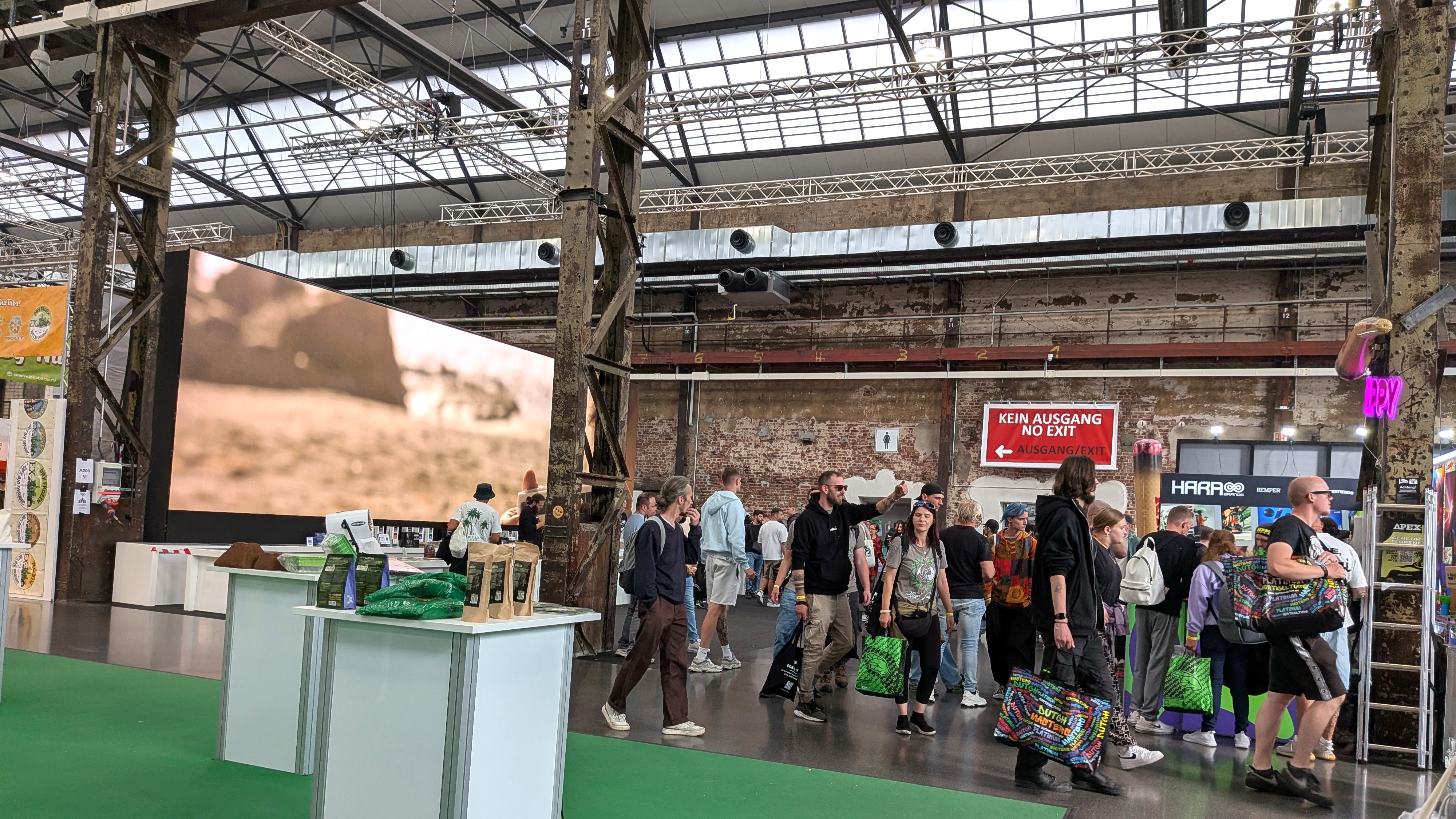Besucher gehen zwischen Messeständen und großen Bildschirmen durch die historische Industriehalle des Areal Böhler in Düsseldorf.