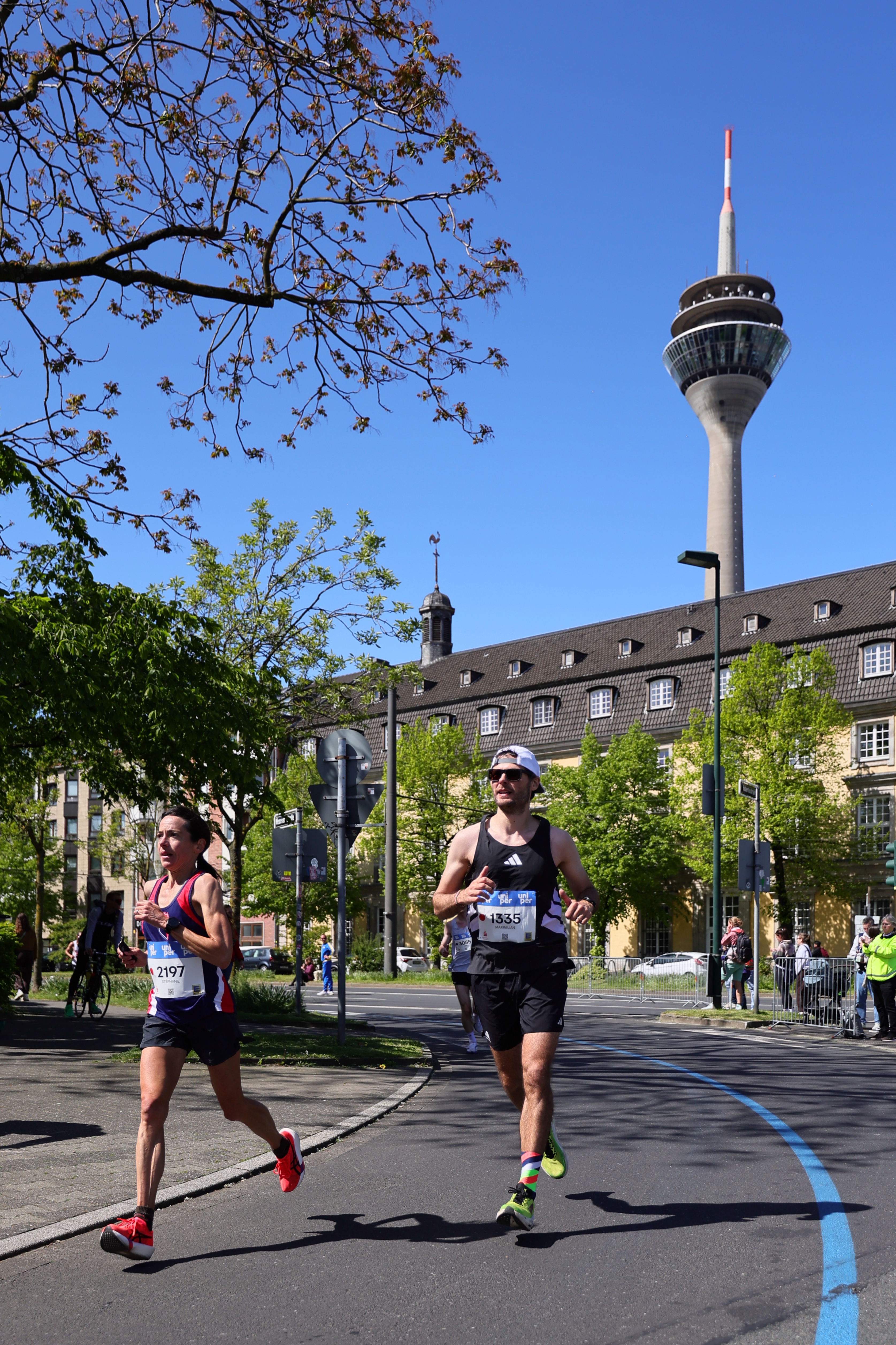 Zwei Läufer beim Uniper Düsseldorf Marathon 2026 mit dem Rheinturm im Hintergrund bei blauem Himmel