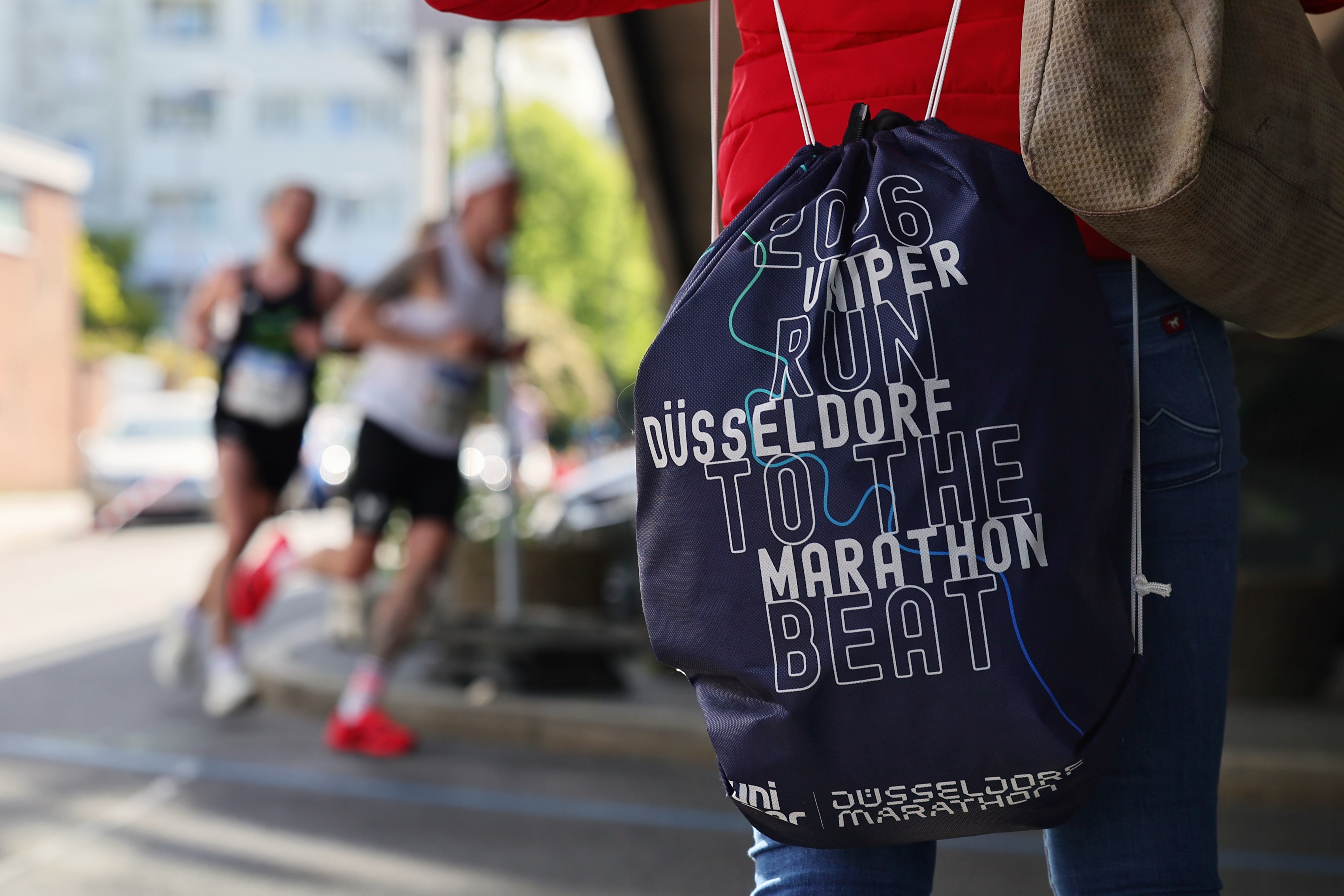 Zuschauerin mit offiziellem Rucksack „2026 Uniper Run to the Beat Düsseldorf Marathon" am Streckenrand