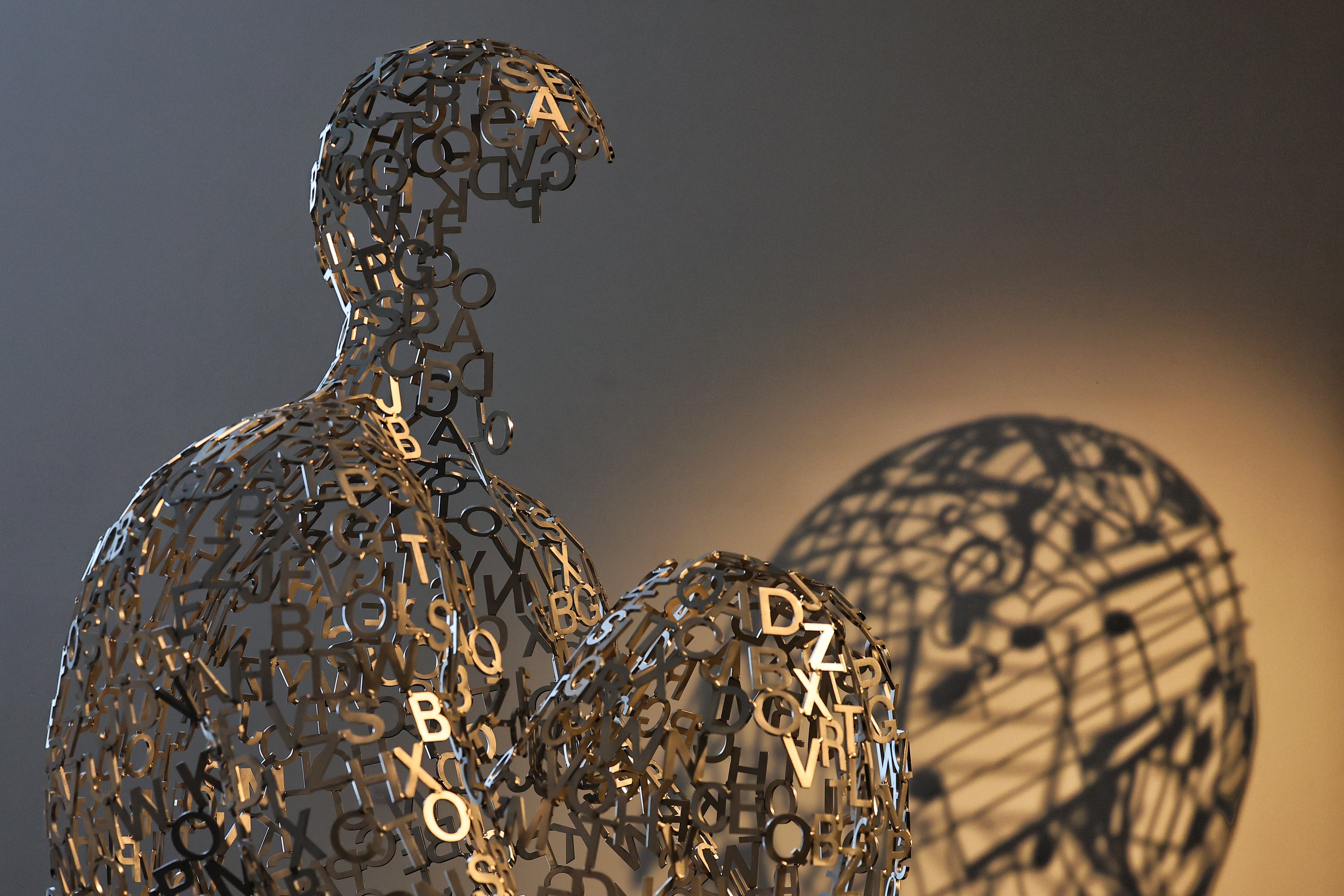 Buchstabenfigur mit Schattenwurf Eine menschliche Skulptur aus verbundenen Buchstaben und Zeichen wirft im Ausstellungsraum des MKM einen großflächigen Schatten an die Wand.