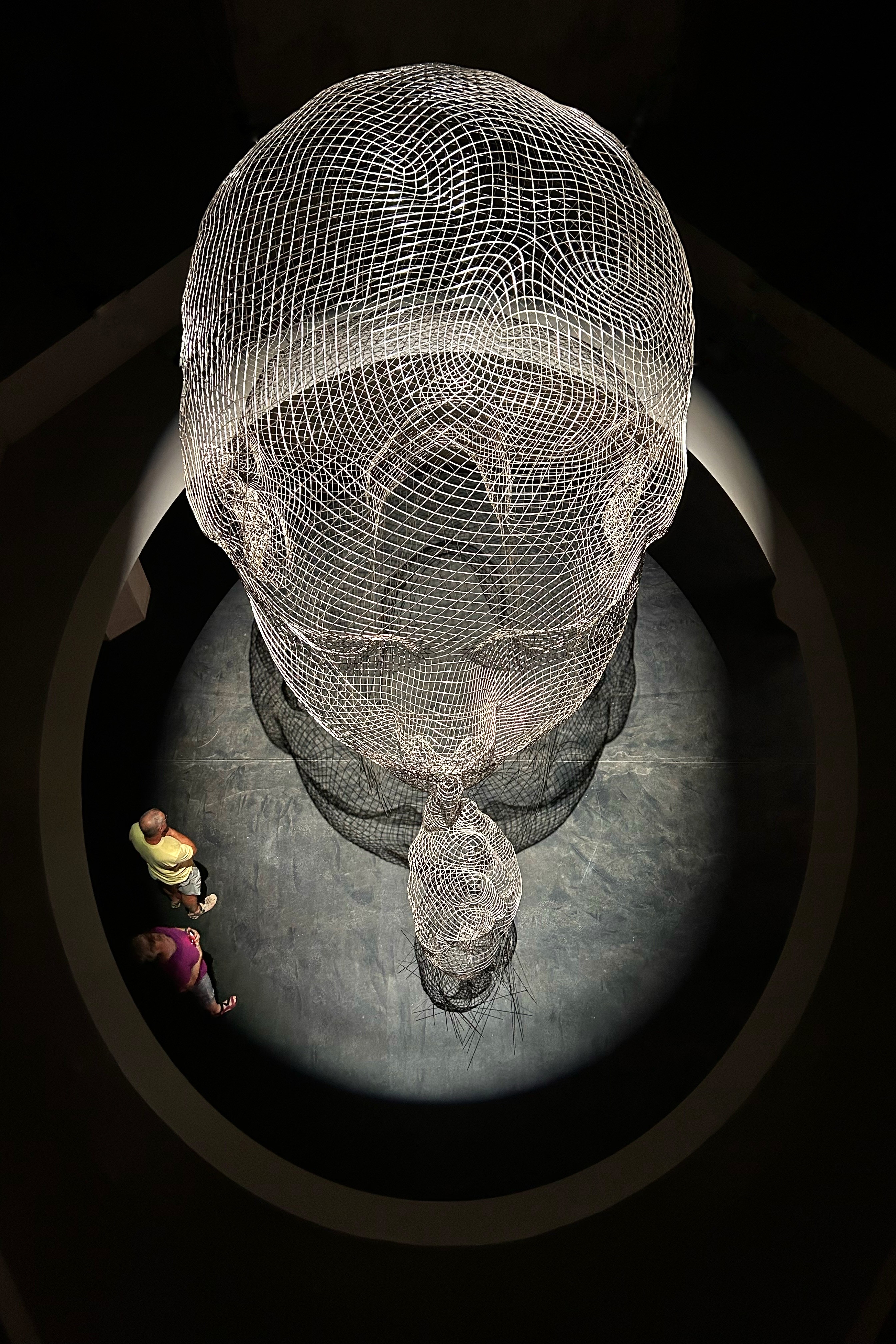 „Invisible Anna“ aus erhöhter Perspektive Blick von oben auf den transparenten Stahlkopf „Invisible Anna“ im Siloraum; eine Person am unteren Bildrand zeigt die monumentale Größe der Skulptur.