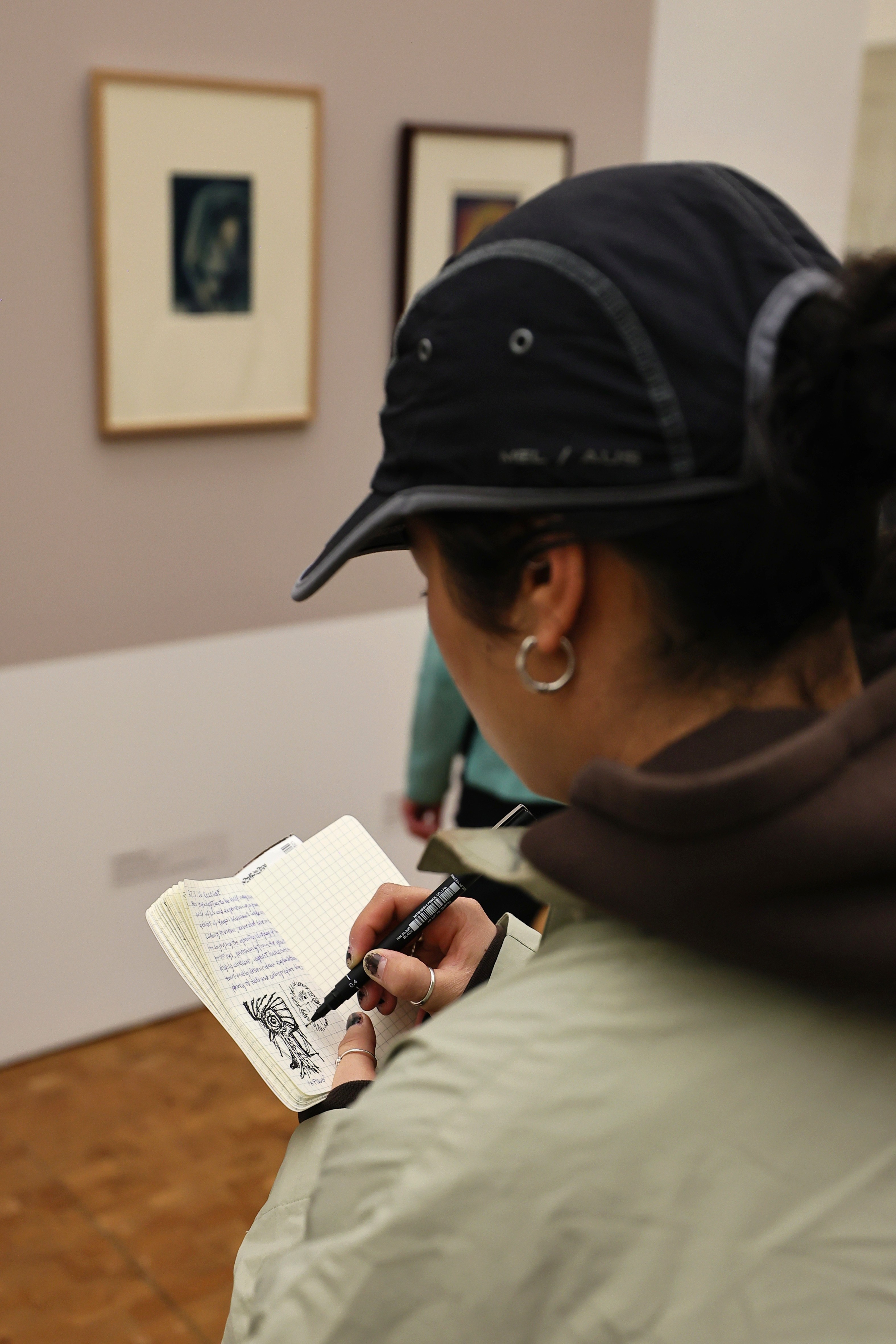 Besucherin skizziert in Notizbuch vor gerahmten Frühwerken in der Kusama-Retrospektive, Museum Ludwig Köln 2026