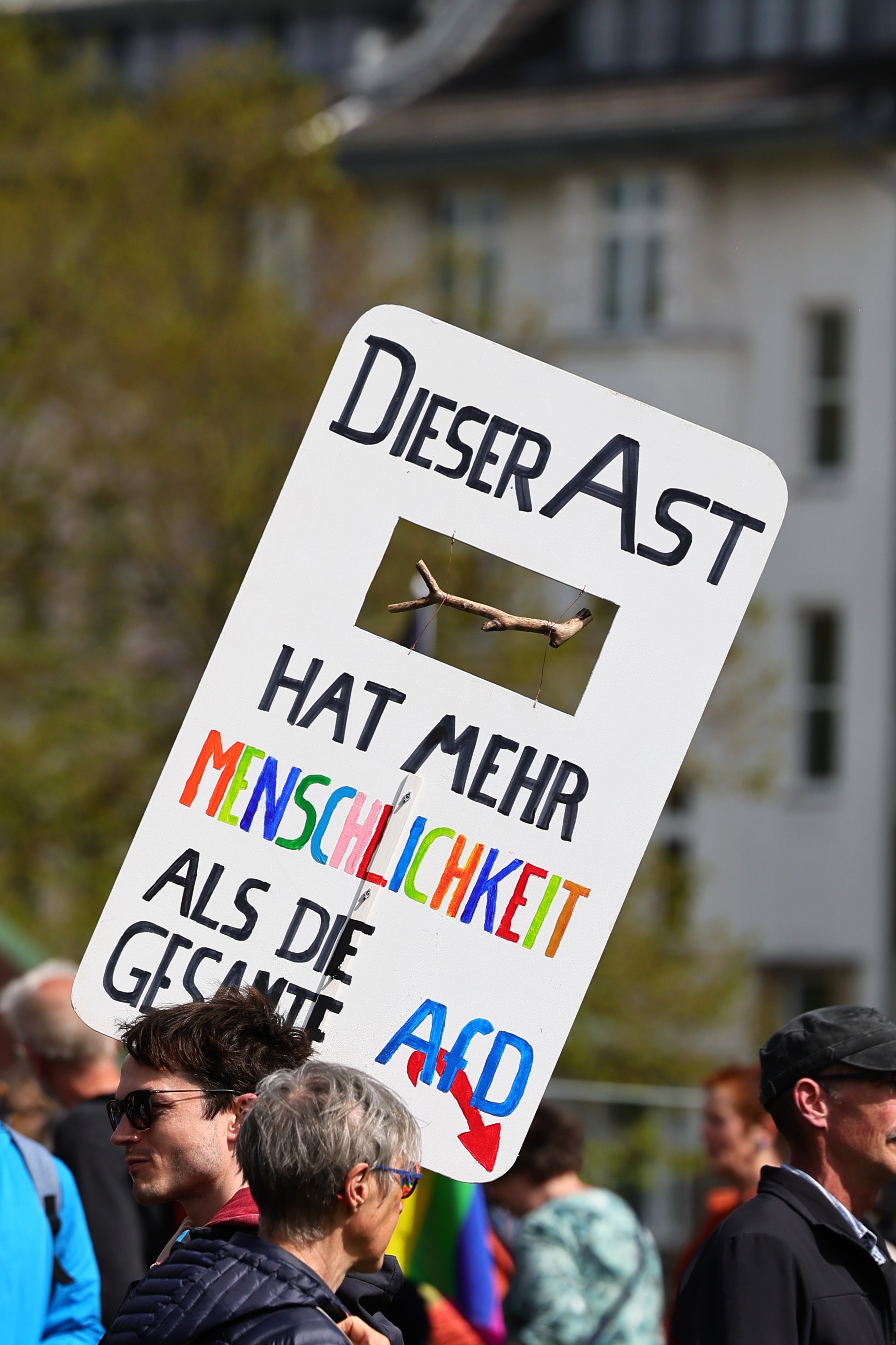 Demonstrant hält Schild mit echtem Ast und der Aufschrift „Dieser Ast hat mehr Menschlichkeit als die gesamte AfD" bei der PRÜF-Demo in Düsseldorf