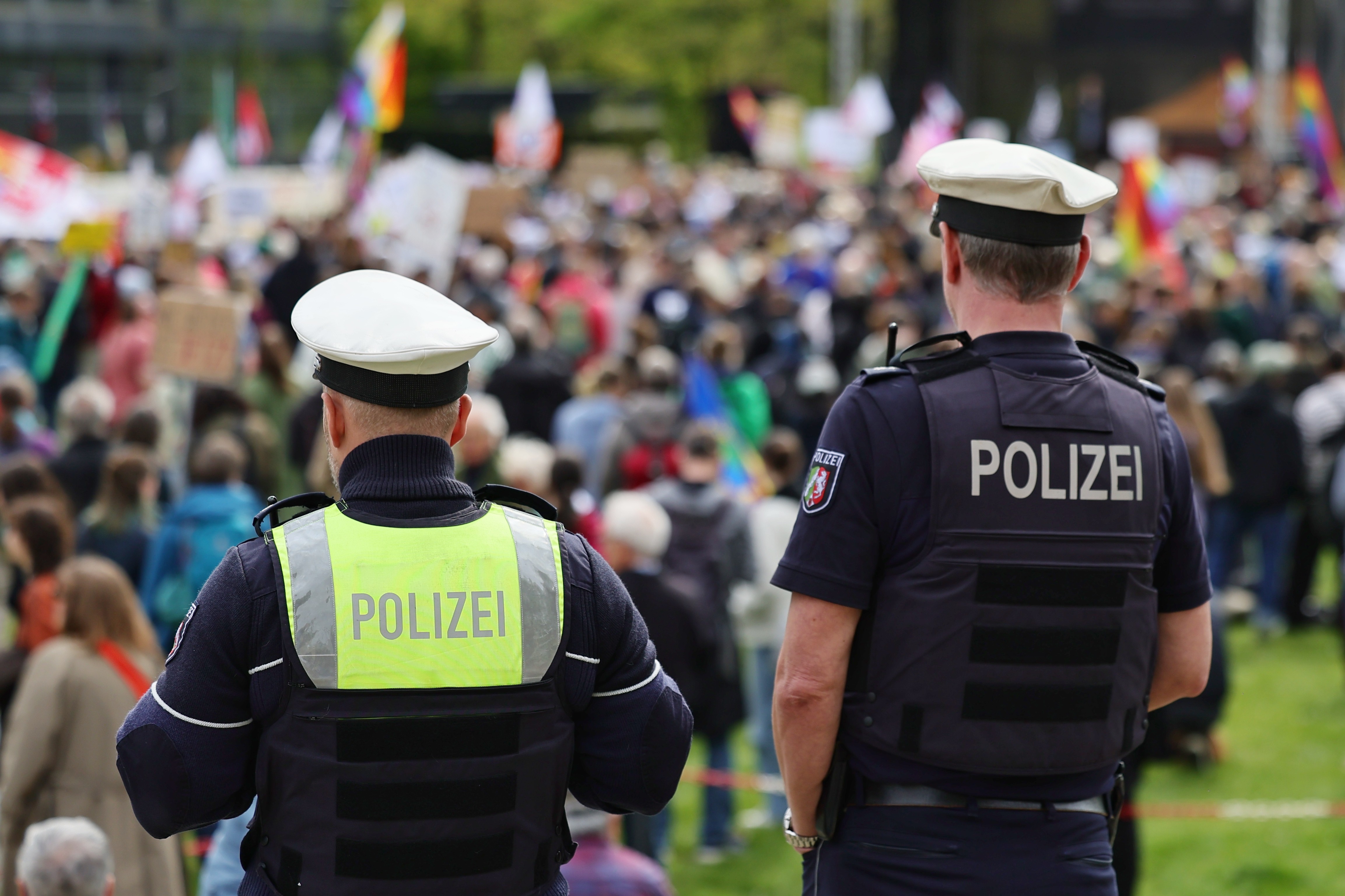 Zwei Polizeibeamte von hinten beobachten die Menge bei der PRÜF-Demo auf der Landtagswiese Düsseldorf am 11. April 2026