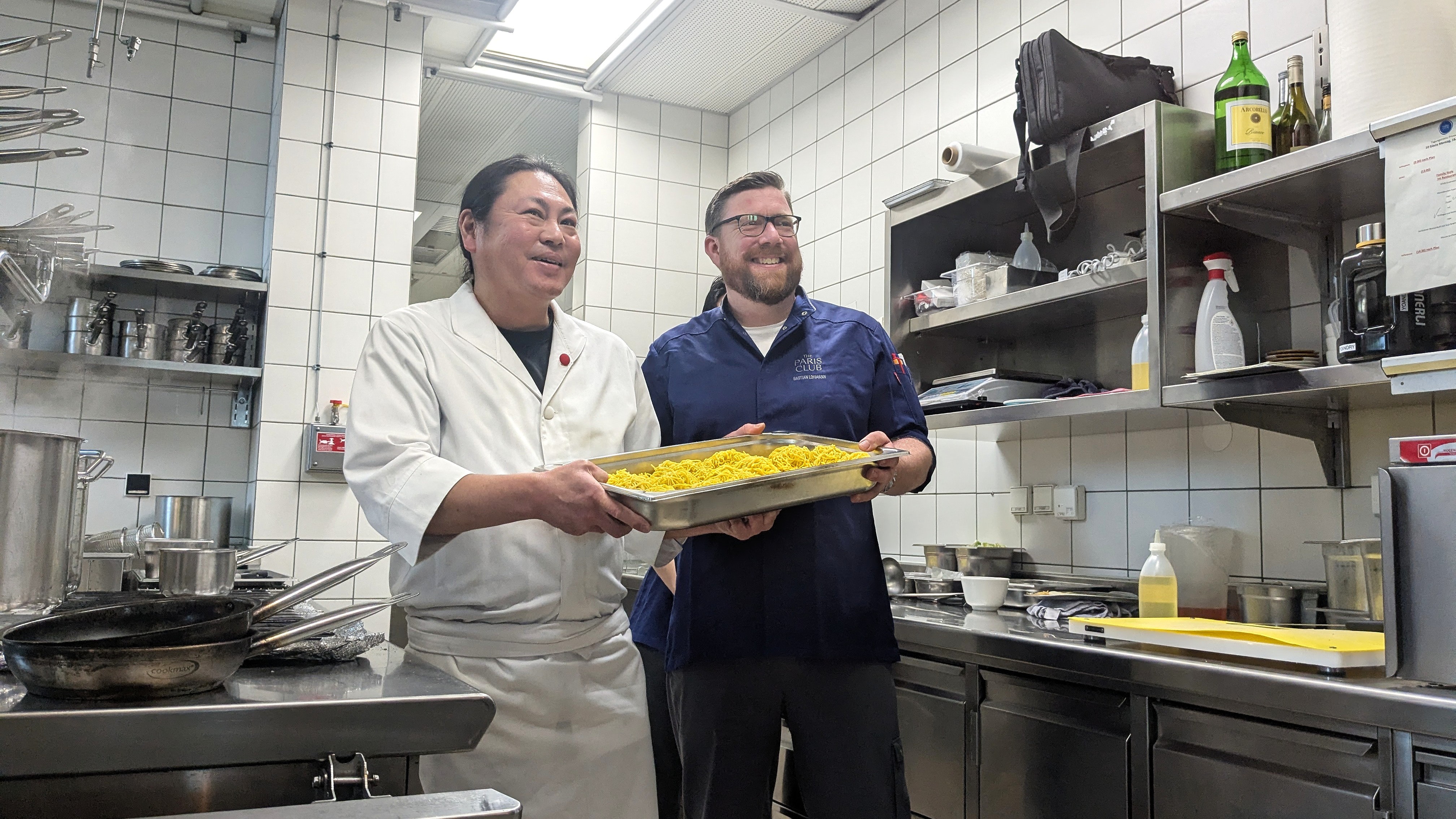 Ryo Kawamura und Bastian Lohmann in der Küche des The Paris Club Küchenchefs Ryo Kawamura von TAKUMI und Bastian Lohmann vom The Paris Club halten gemeinsam ein Blech mit Ramen-Nudeln in der Küche