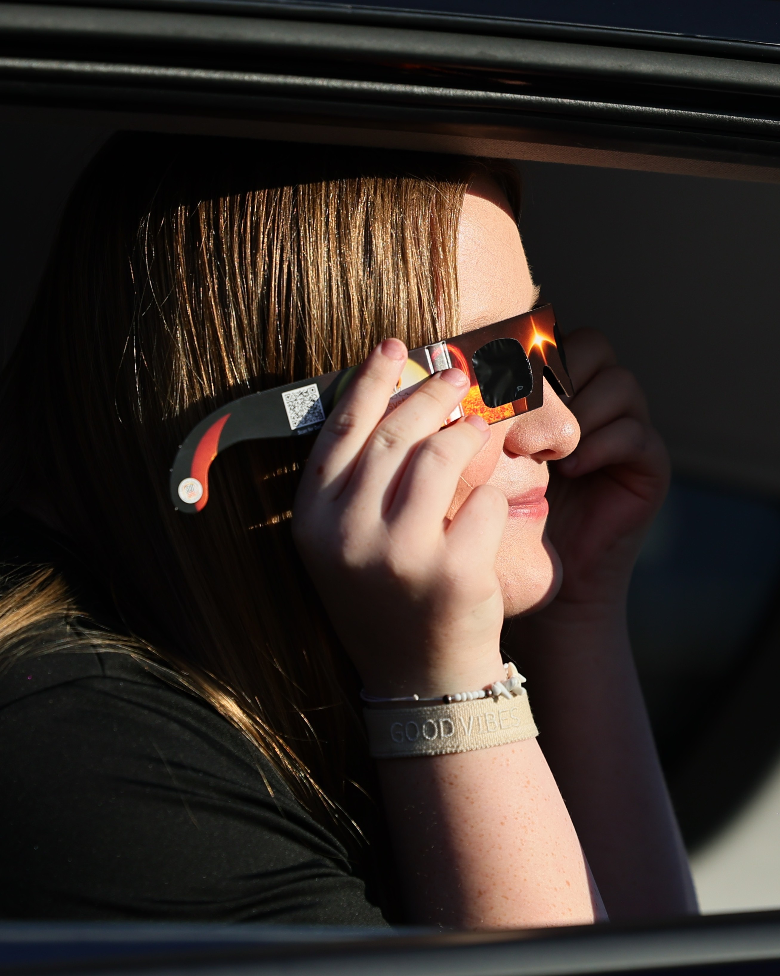 Eine Frau betrachtet die Sonnenfinsternis mit einer speziellen Schutzbrille aus einem geöffneten Autofenster.